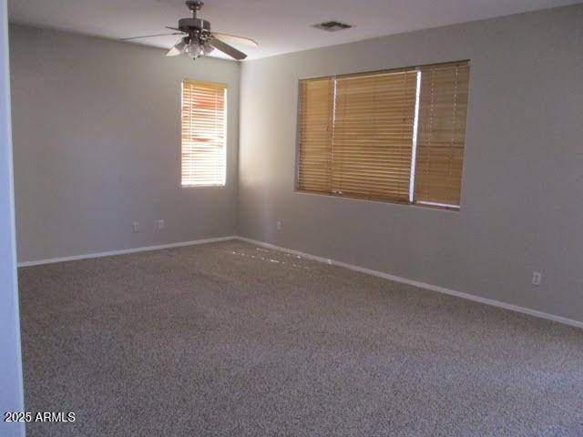 empty room with carpet floors, visible vents, baseboards, and a ceiling fan