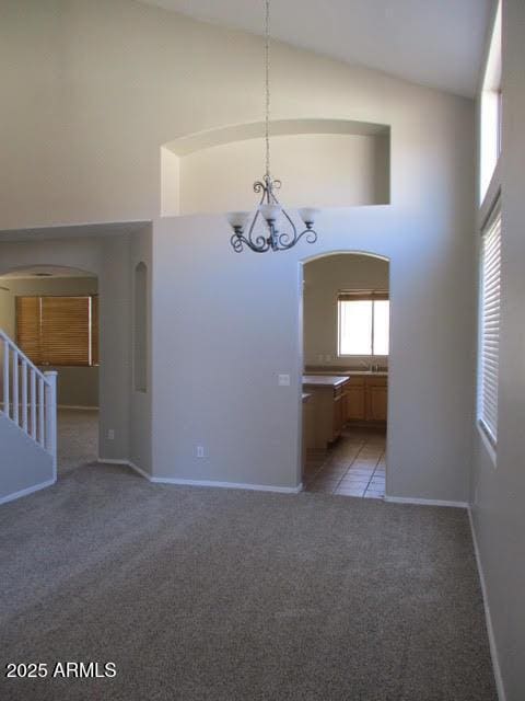 unfurnished dining area with arched walkways, high vaulted ceiling, light carpet, baseboards, and an inviting chandelier