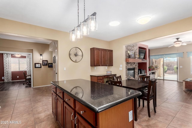 kitchen with ceiling fan, a fireplace, dark stone countertops, pendant lighting, and a center island