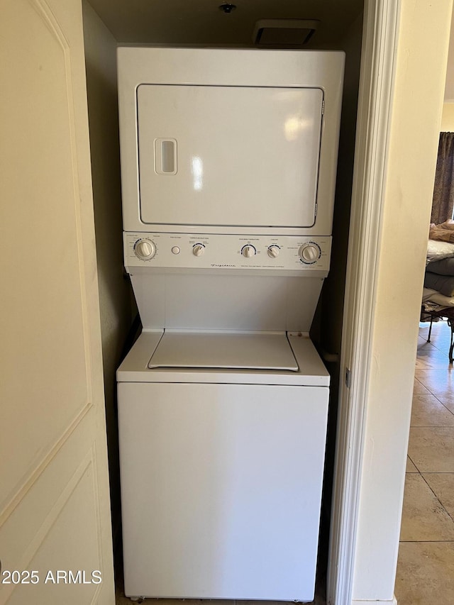 clothes washing area featuring light tile patterned floors and stacked washer and clothes dryer