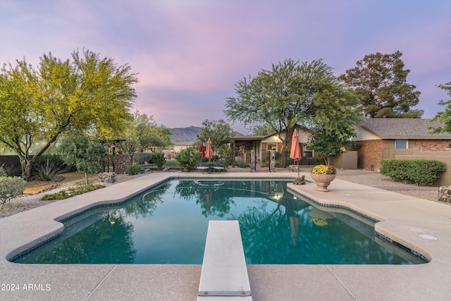 pool at dusk with a patio and a diving board