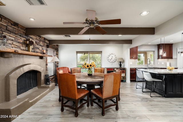 dining area featuring a fireplace, beam ceiling, light wood-type flooring, and ceiling fan