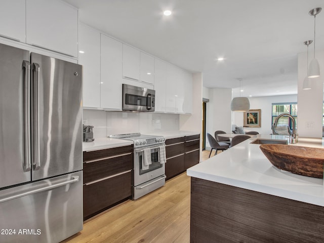 kitchen featuring appliances with stainless steel finishes, white cabinetry, pendant lighting, light hardwood / wood-style floors, and dark brown cabinetry