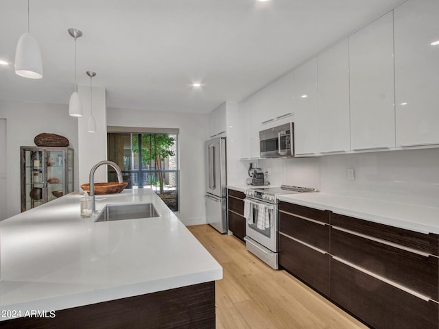 kitchen featuring light wood finished floors, modern cabinets, stainless steel appliances, white cabinetry, and a sink