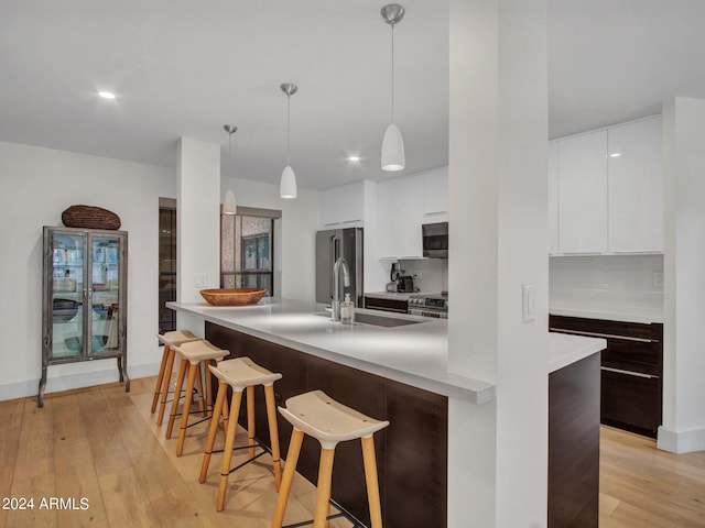 kitchen featuring a breakfast bar area, white cabinetry, appliances with stainless steel finishes, light wood finished floors, and modern cabinets