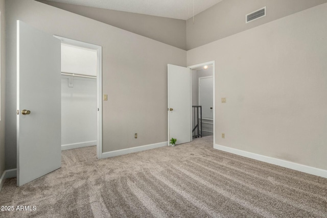 unfurnished bedroom featuring carpet, visible vents, baseboards, vaulted ceiling, and a walk in closet