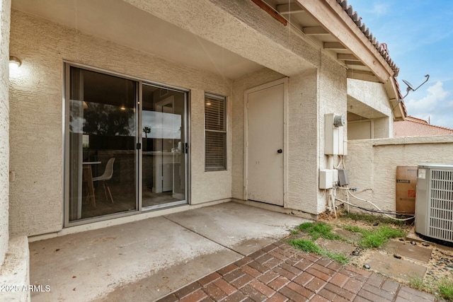 entrance to property featuring stucco siding, cooling unit, and a patio