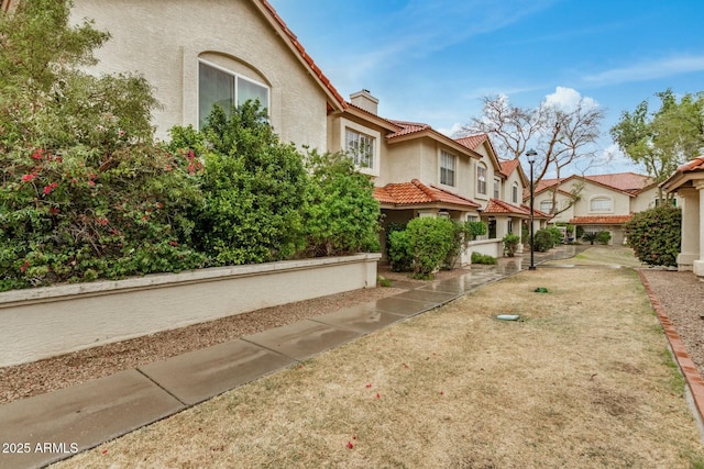 view of side of property featuring a tiled roof, a chimney, a residential view, and stucco siding