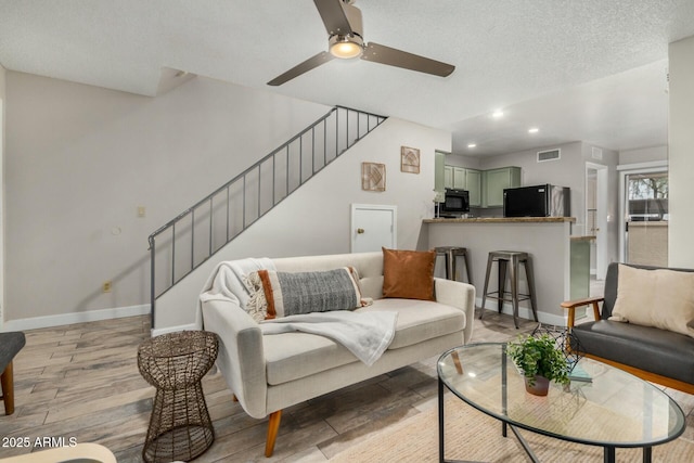 living room with stairway, a textured ceiling, baseboards, and light wood-style floors