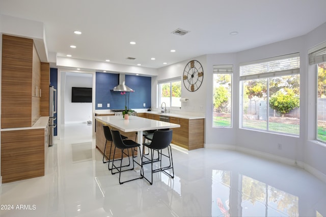 kitchen featuring light tile patterned flooring, a kitchen island, sink, a breakfast bar area, and wall chimney exhaust hood