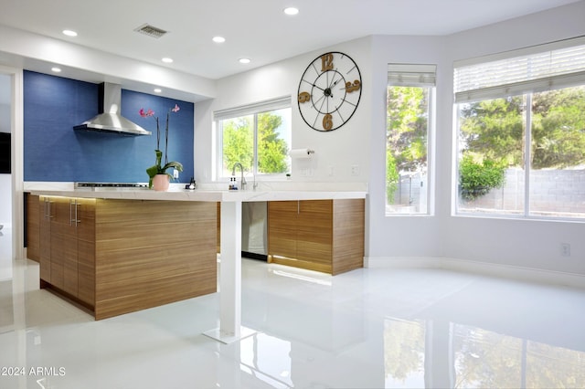 kitchen with sink, a wealth of natural light, stovetop, and wall chimney range hood