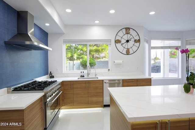 kitchen with sink, backsplash, light stone counters, stainless steel appliances, and wall chimney exhaust hood