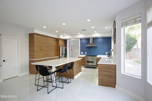 kitchen featuring wall chimney range hood, sink, a breakfast bar area, high end appliances, and a kitchen island