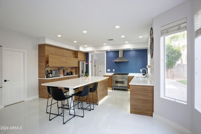 kitchen featuring sink, a kitchen bar, premium appliances, a center island, and wall chimney range hood