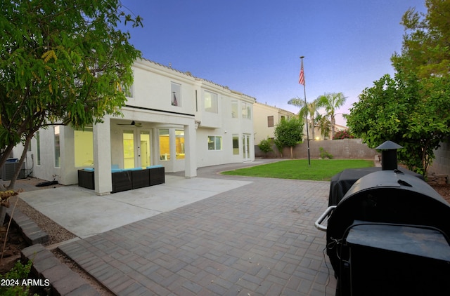 back house at dusk featuring central AC, a patio area, a yard, ceiling fan, and an outdoor hangout area