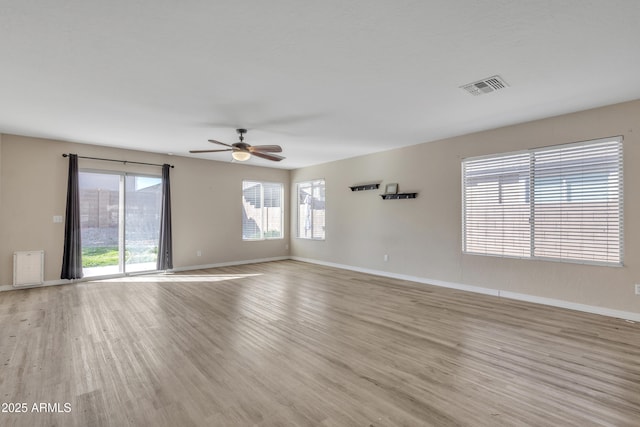 empty room featuring a ceiling fan, wood finished floors, visible vents, and baseboards