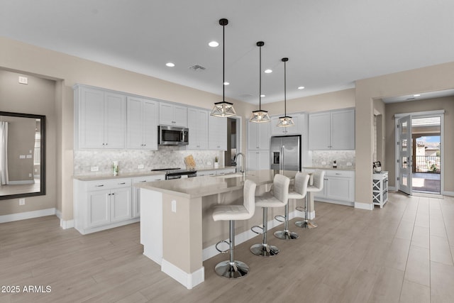 kitchen with sink, a breakfast bar, a kitchen island with sink, stainless steel appliances, and decorative light fixtures