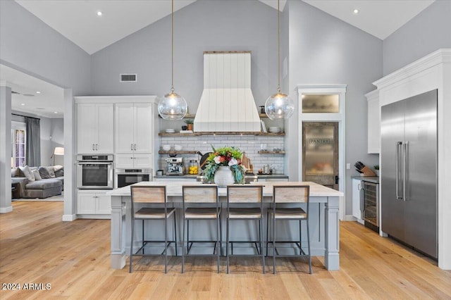 kitchen with appliances with stainless steel finishes, extractor fan, pendant lighting, high vaulted ceiling, and white cabinetry