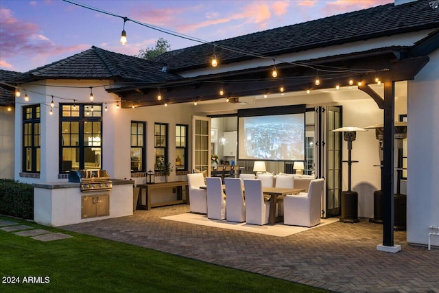 back house at dusk featuring exterior kitchen and a patio