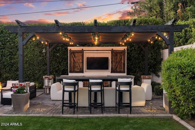 patio terrace at dusk with a pergola, an outdoor living space with a fireplace, and an outdoor bar