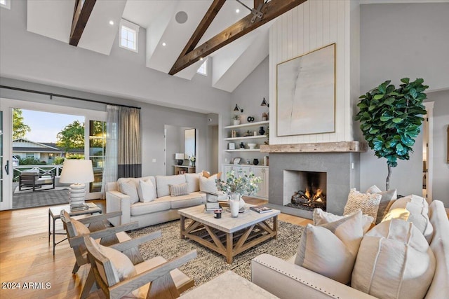 living room with beamed ceiling, a large fireplace, high vaulted ceiling, and light hardwood / wood-style flooring