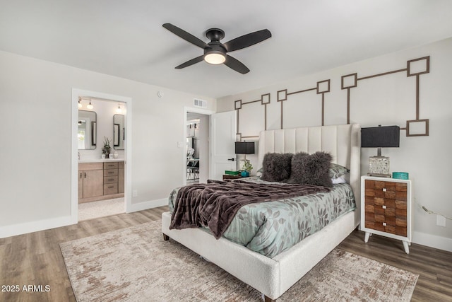 bedroom featuring wood finished floors, baseboards, ensuite bath, and ceiling fan