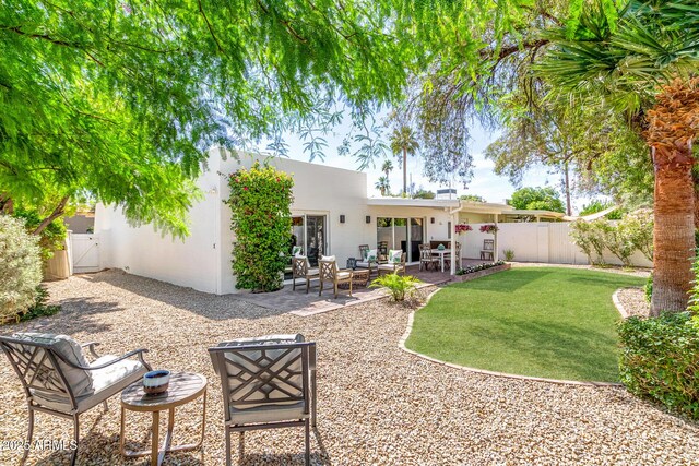 rear view of house featuring stucco siding, a patio area, and a gate
