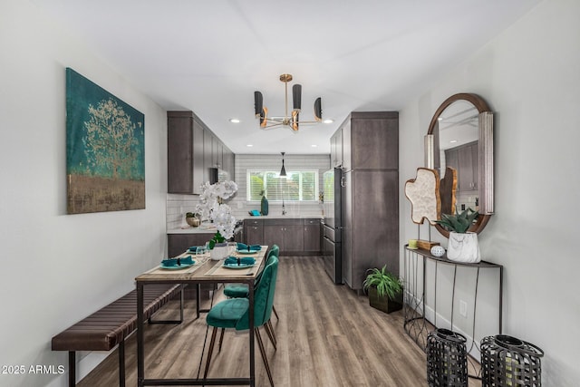 kitchen featuring light wood-style floors, a chandelier, backsplash, dark brown cabinets, and a sink