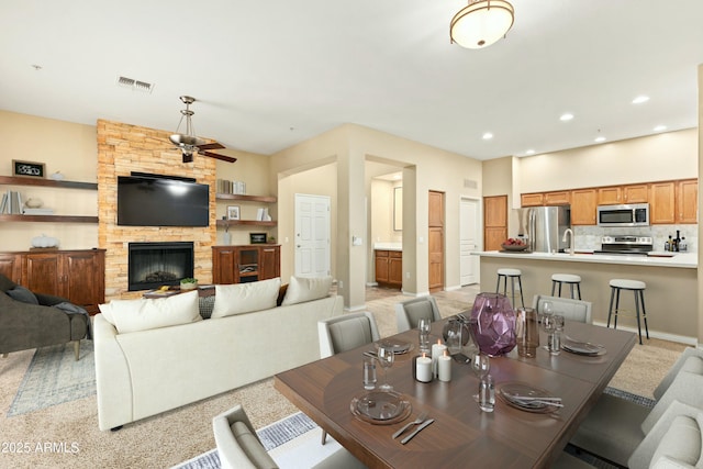 dining room featuring a stone fireplace, ceiling fan, and sink