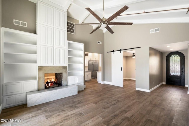 unfurnished living room featuring beamed ceiling, a barn door, wood-type flooring, and a premium fireplace