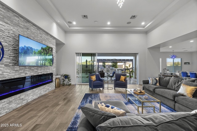 living room with hardwood / wood-style flooring, a towering ceiling, and a stone fireplace