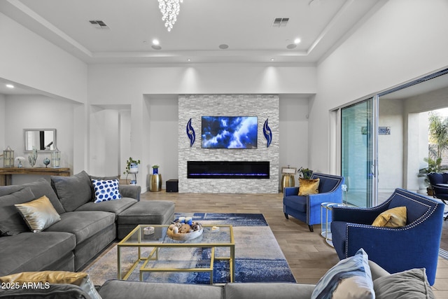 living room with hardwood / wood-style flooring, a tray ceiling, and a stone fireplace