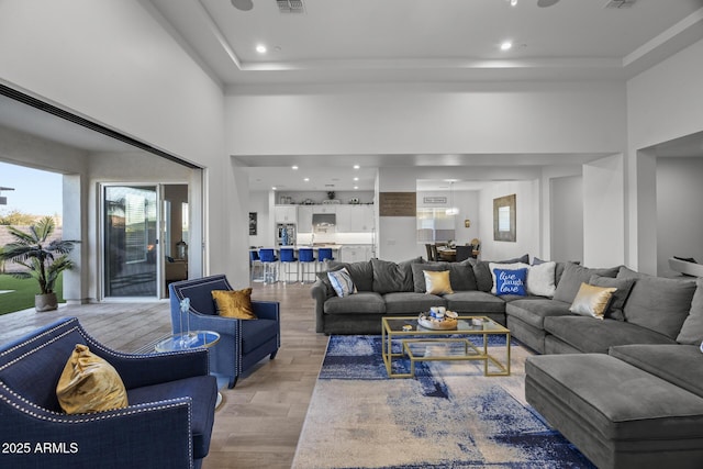 living room featuring a towering ceiling, a raised ceiling, and light hardwood / wood-style flooring