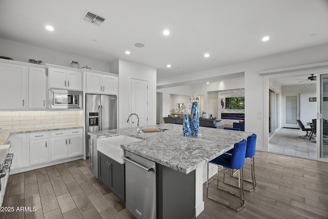 kitchen featuring high quality appliances, white cabinetry, a kitchen island with sink, and sink