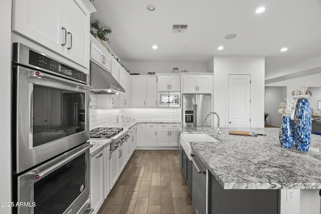 kitchen with tasteful backsplash, white cabinetry, a large island, light stone counters, and stainless steel appliances