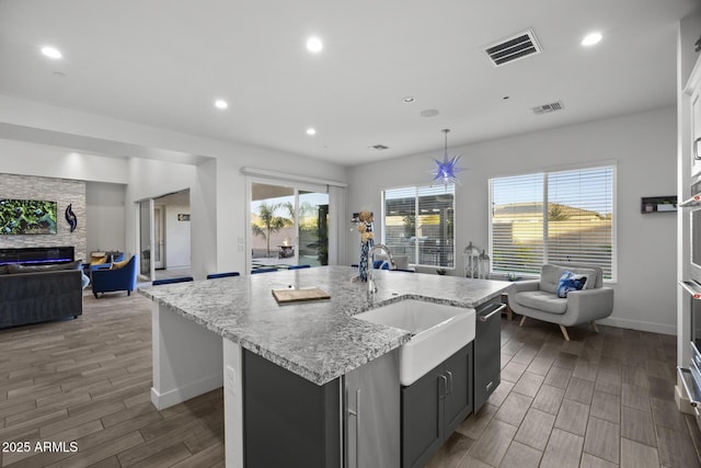 kitchen featuring sink, a stone fireplace, stainless steel appliances, an island with sink, and decorative light fixtures