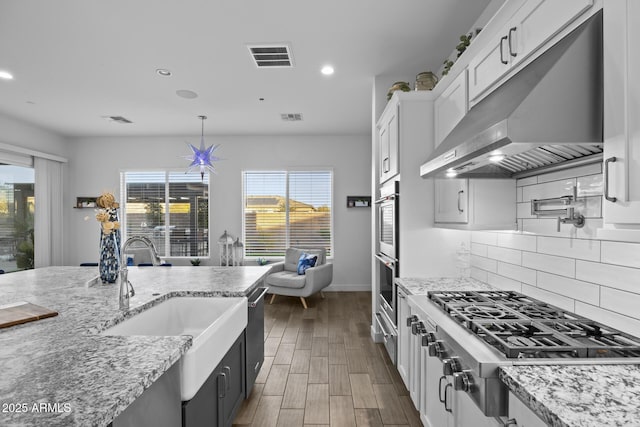 kitchen with stainless steel appliances, wall chimney range hood, and white cabinets