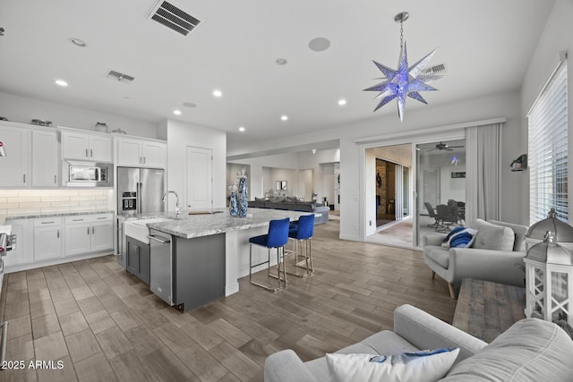 kitchen featuring a kitchen bar, sink, an island with sink, stainless steel appliances, and white cabinets