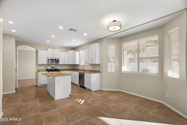 kitchen featuring tile patterned floors, appliances with stainless steel finishes, sink, white cabinets, and a center island