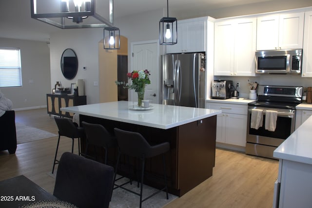 kitchen featuring appliances with stainless steel finishes, a center island, white cabinets, and decorative light fixtures