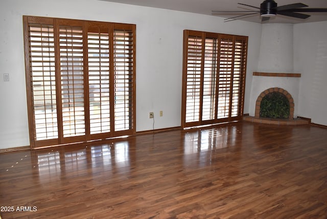 unfurnished living room with ceiling fan, a fireplace, and dark wood-type flooring