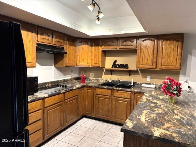 kitchen featuring dark stone counters, black appliances, a raised ceiling, sink, and light tile patterned flooring