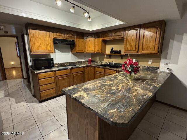 kitchen featuring kitchen peninsula, dark stone counters, a raised ceiling, light tile patterned floors, and stainless steel gas stovetop