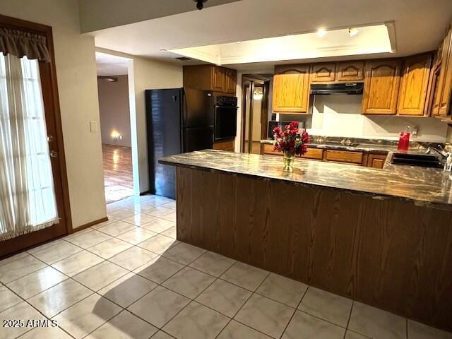 kitchen featuring kitchen peninsula, a tray ceiling, black appliances, sink, and light tile patterned floors