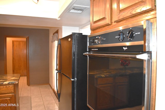 kitchen with black fridge, light tile patterned floors, and oven