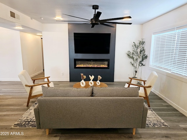 living area with wood finished floors, a ceiling fan, visible vents, baseboards, and a glass covered fireplace