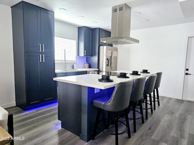 kitchen featuring island range hood, stainless steel fridge with ice dispenser, a center island, light countertops, and a sink