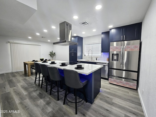 kitchen featuring island exhaust hood, stainless steel appliances, light countertops, visible vents, and a kitchen breakfast bar