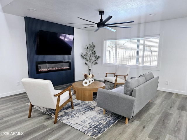 living area with baseboards, wood finished floors, and a glass covered fireplace