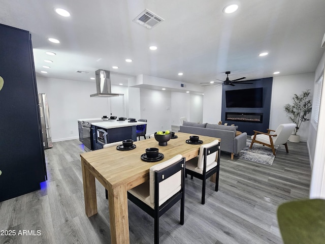 dining space with light wood finished floors, visible vents, a ceiling fan, a fireplace, and recessed lighting